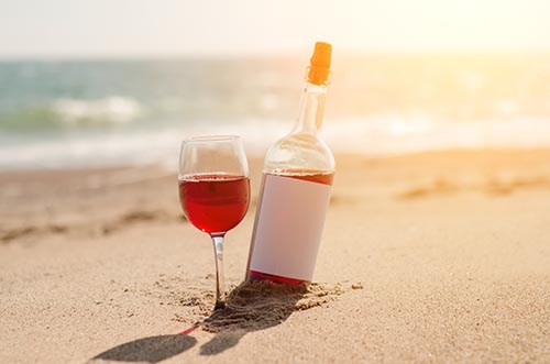 Glass of red rose wine and bottle on the beach at the summer sunny day. Sea on the background